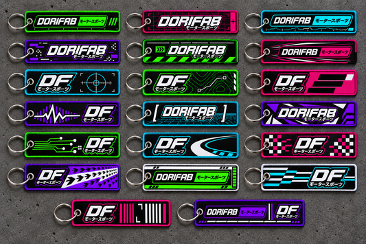 All 20 Dorifab Motorsport flight tag keyring designs laid out on a charcoal tabletop